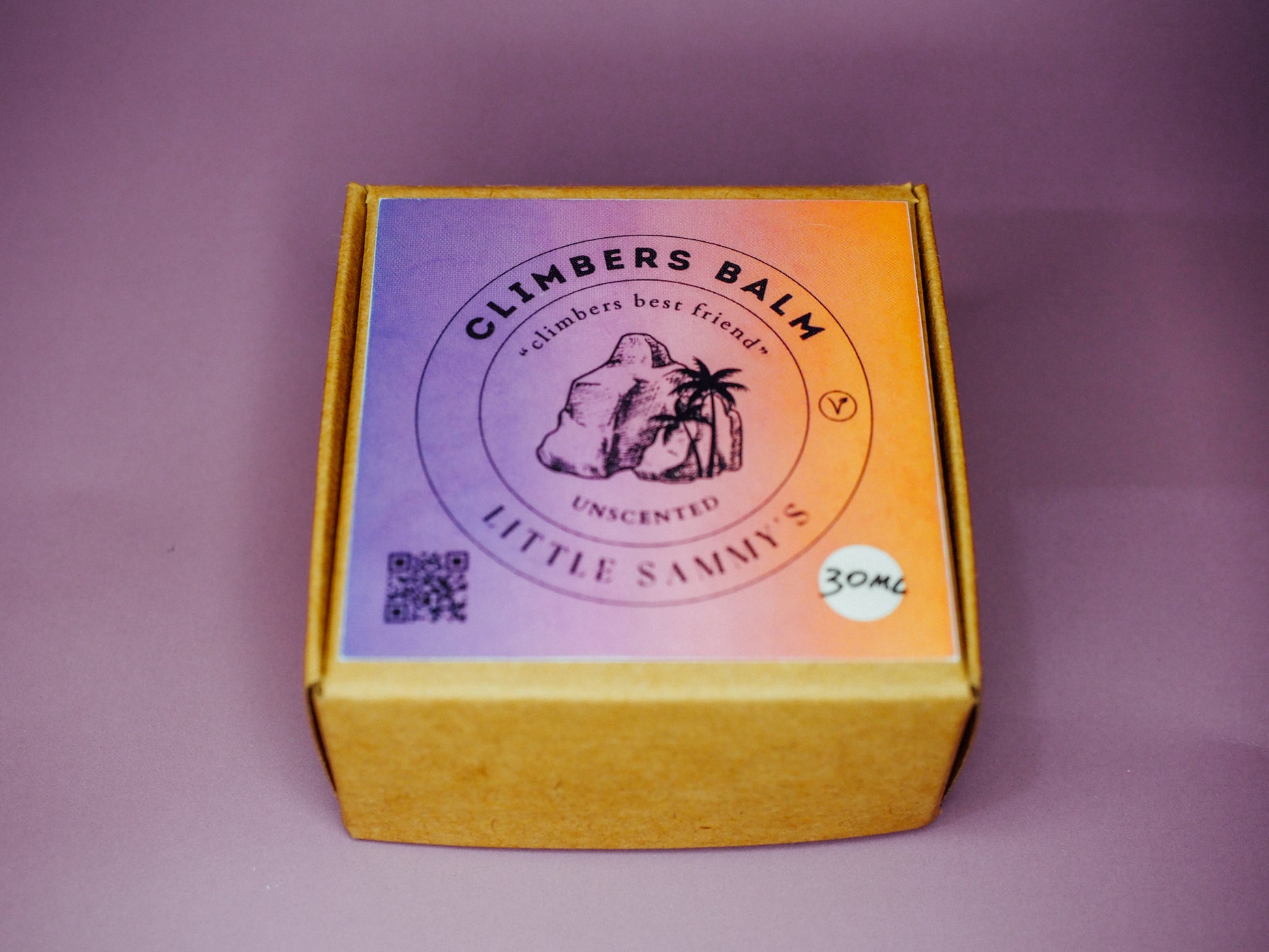 A closed premium kraft box for Little Sammy's Unscented Climbers Balm Travel Bundle, featuring a crisp label with a QR code, sits against a light purple backdrop, hinting at the quality skincare journey within for climbers.