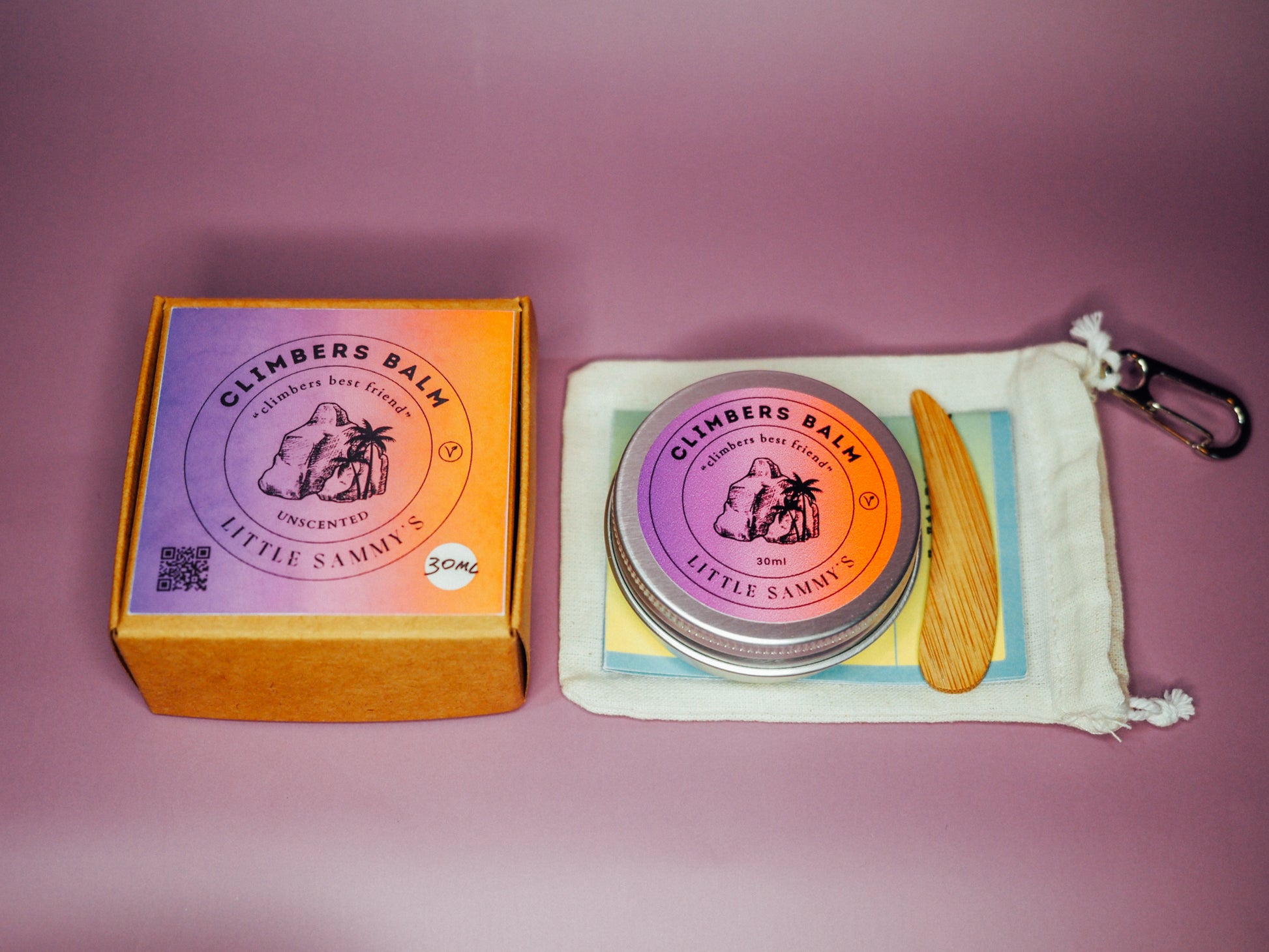 An unscented travel bundle from Little Sammy's Climbers Balm, consisting of a 30ml tin displayed alongside a drawstring calico cotton bag with a wooden spatula and carabiner, set against a light purple background. The focus is on the product contents and kraft box with vibrant labelling showcasing the product.